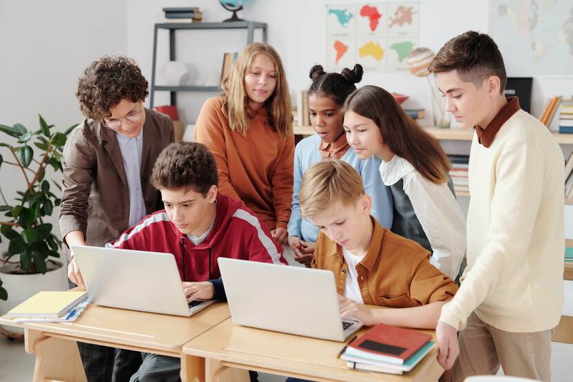 Een groep tieners in een klaslokaal. Samen staan ze om 2 laptops heen.